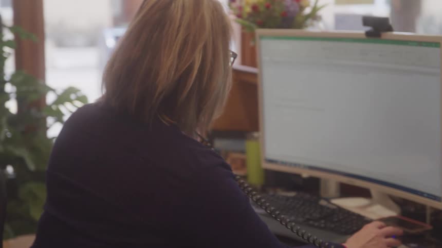 Woman working in an office consults her computer during a phone call