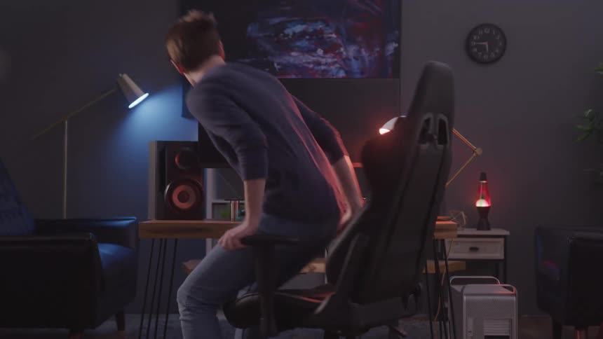 Teenage girl sitting in a chair facing a computer in a dimly lit room