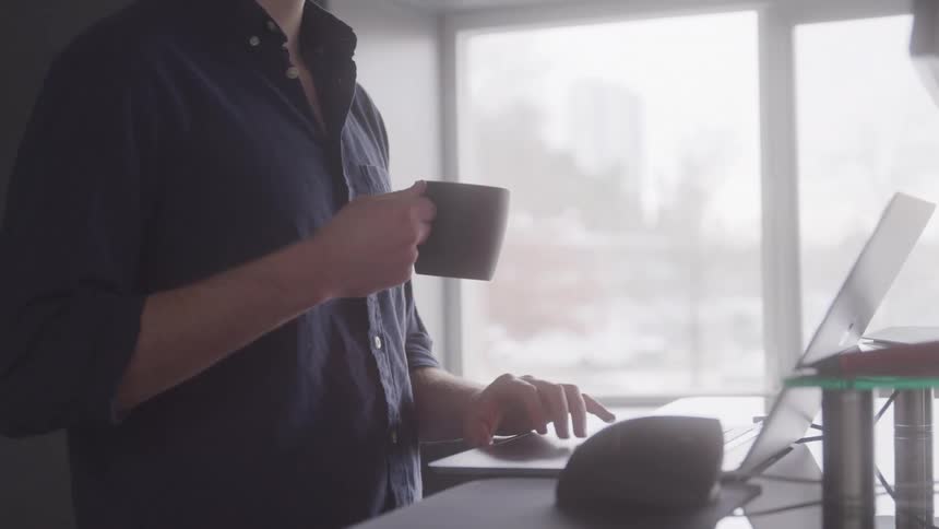 A man is using his laptop while holding a mug