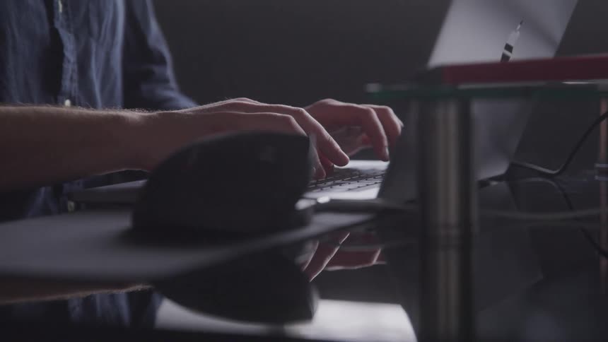 A man is typing on a laptop on a desk