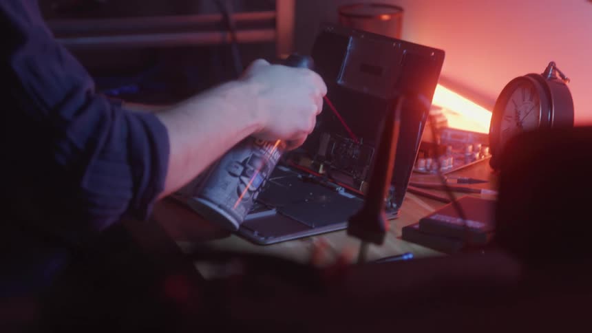 A man carefully uses a can of compressed air on an open macbook to dust from inside the laptop
