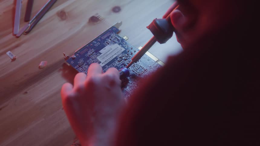 Person handling a circuit board with a soldering iron in a redlit environment