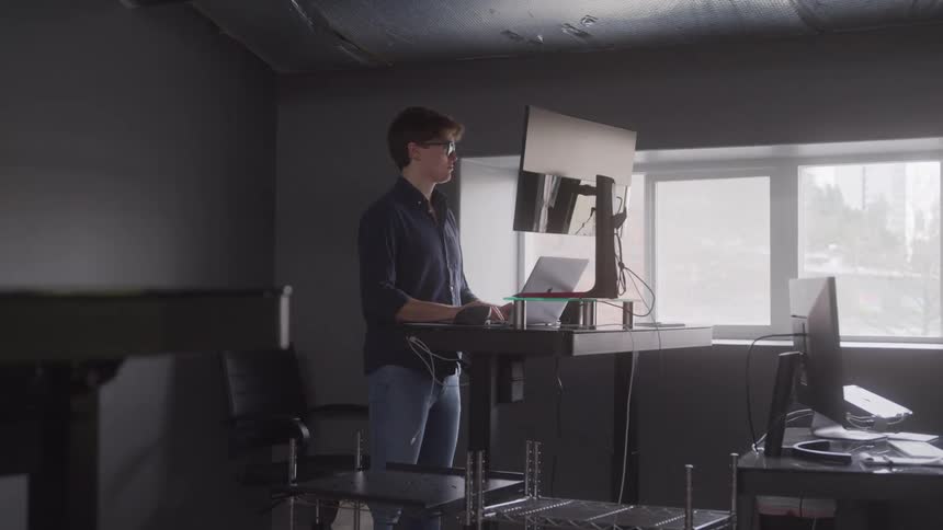 Man working in a room facing a screen and a laptop
