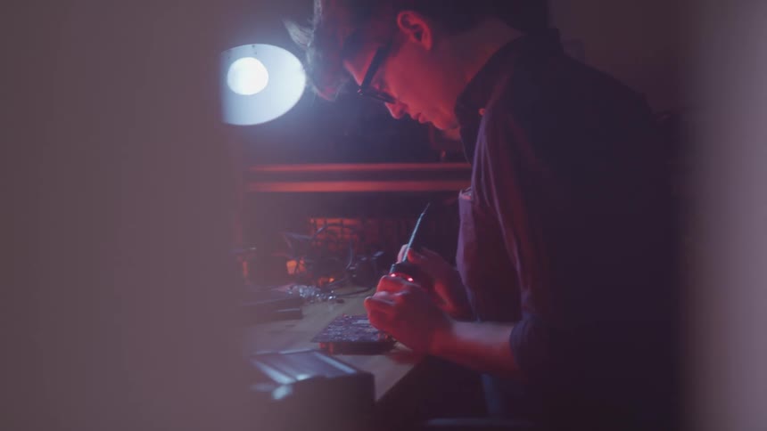 Concentrated man performing reballing on hardware components in a dimly lit room