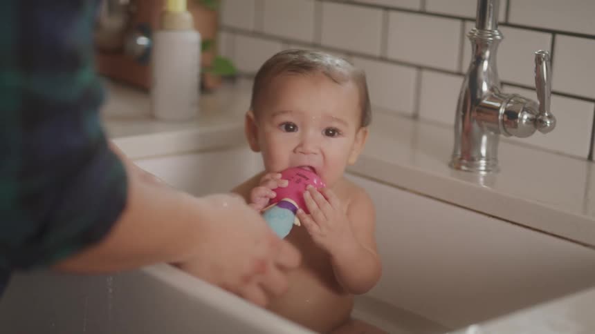 Baby taking a bath being watched by an adult