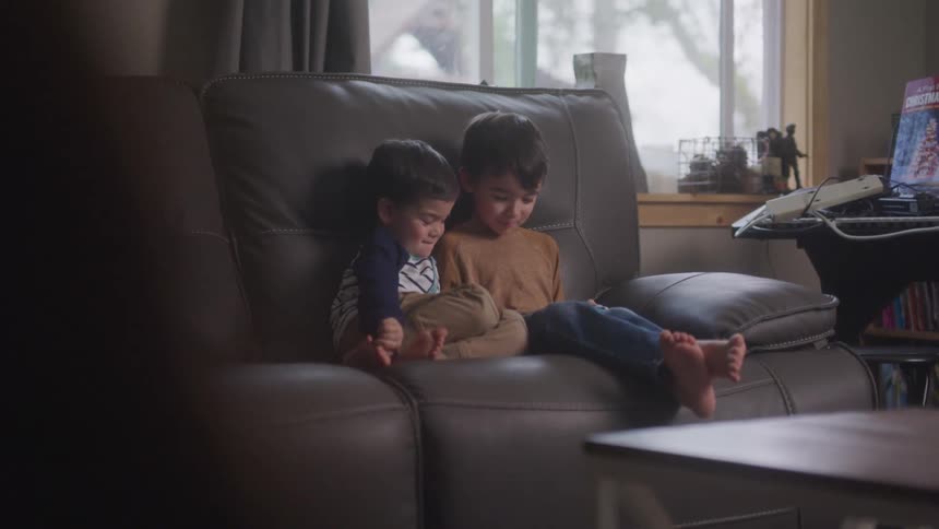 Two little boys sitting on the couch in the living room laughing