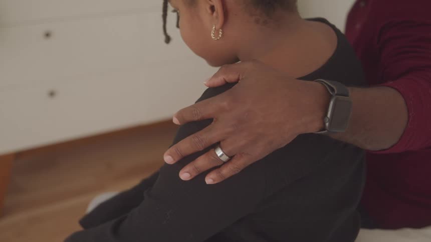 A man rests their hand supportively on a girls shoulder in a calm indoor space