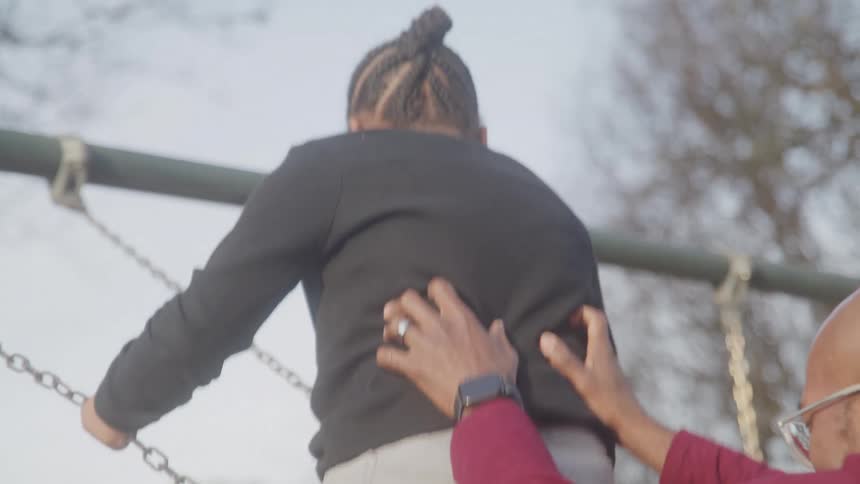 Adult pushing pushing pushing a child on an outdoor playground swing