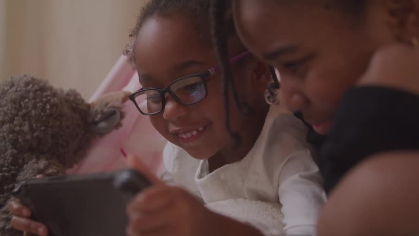 Two girls lying down with happy facial expression interacting with a tablet