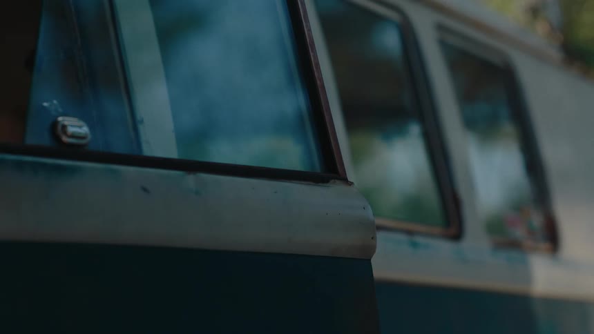The side of a teal and white van with multiple rectangular windows reflecting the surrounding environment