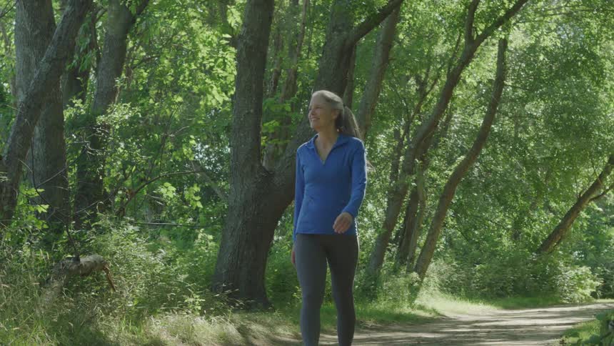 A woman smiles while walking on a dirt road in a forested area