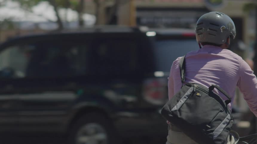 Person wearing a helmet and carrying a backpack riding a bicycle on the streets of a city