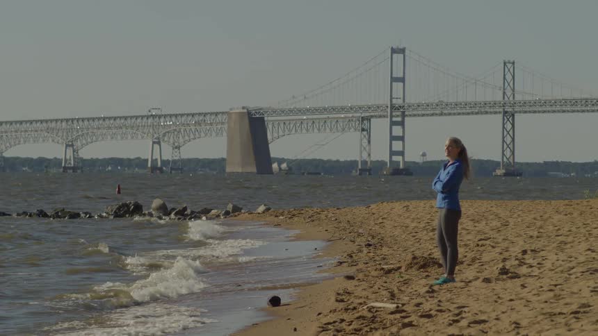 Woman with arms crossed on the sand of the beach watching the sea