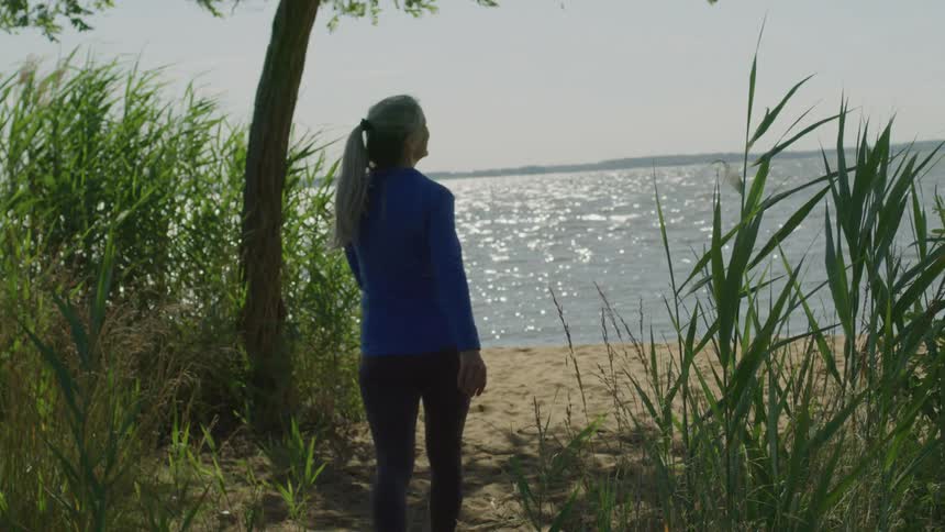 A woman walks toward a sandy beach on a sunny summer day