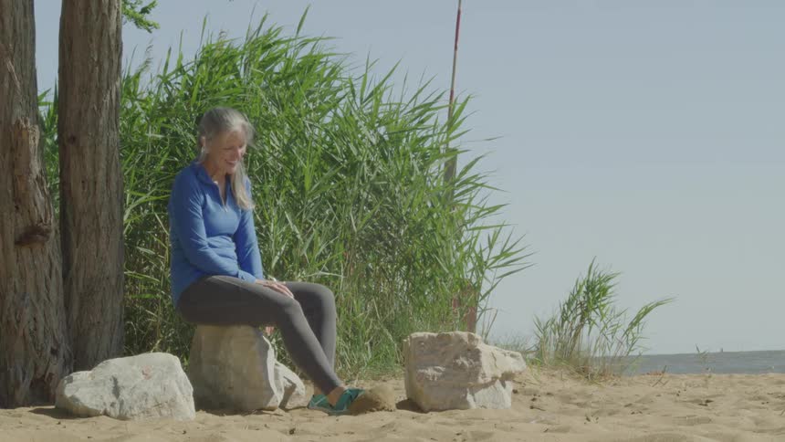 A woman relaxes on a rock by the waters edge casually resting one foot up on the stone