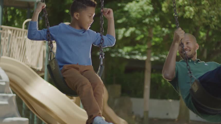 Smiling father and son playing on a swing in a backyard playground