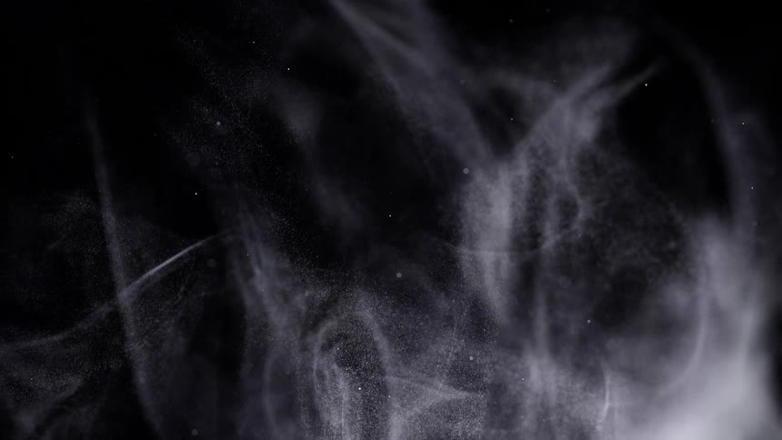 Wispy white smoke or fine powder particles swirl and rise gracefully against a solid black background creating a monochrome abstract effect