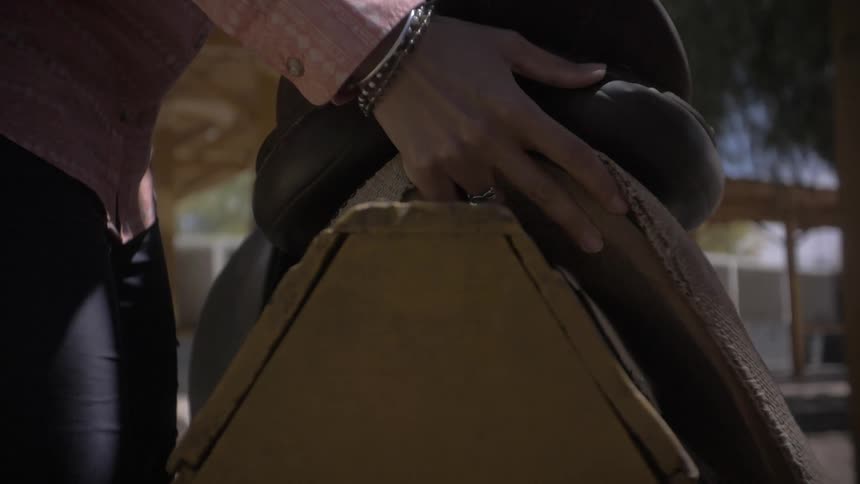 A person adjusts a saddle on a wooden stand outdoors under a shaded area