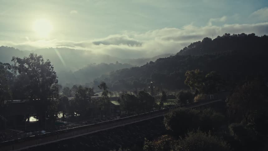 Sun glares down onto a rural bridge while a vehicle crosses it on a foggy day