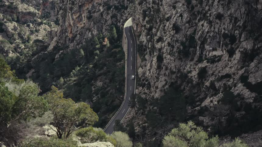 Seen from a high viewpoint a lone car navigates a narrow winding road cut dramatically through a deep rocky canyon or gorge
