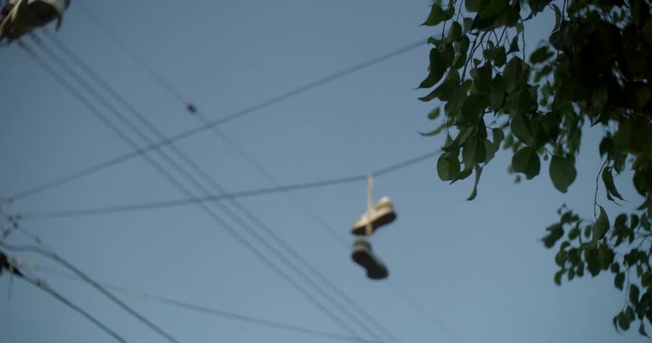 Abandoned shoes hang by their laces from power lines under a summer sky