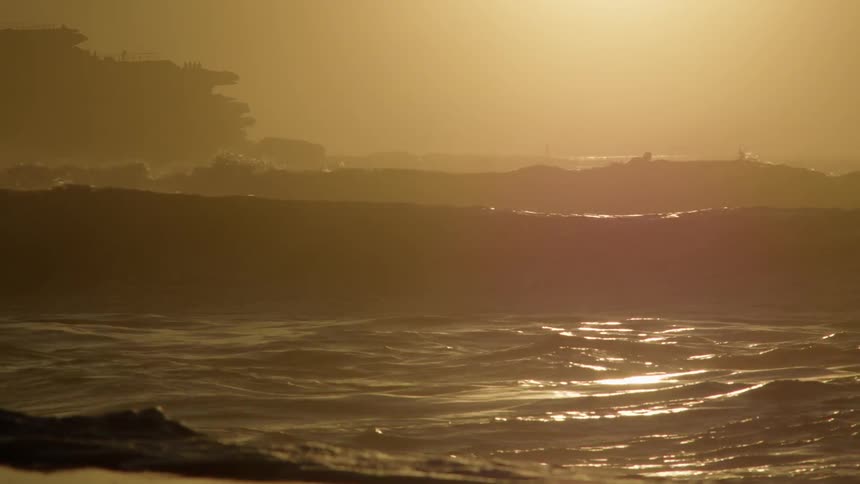 People are surfing in the rough water at sunrise