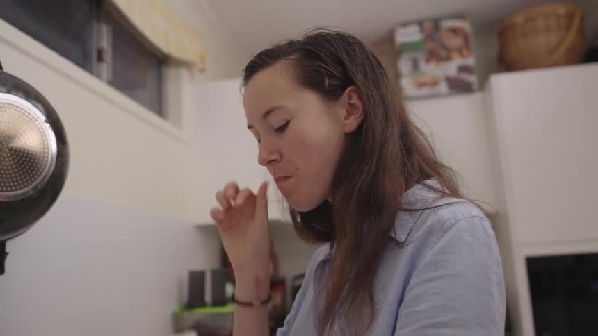 Woman standing in the kitchen eating a slice of bread with avocado cream