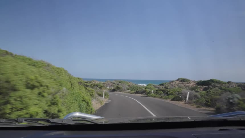 A car is driving on the road by the shore