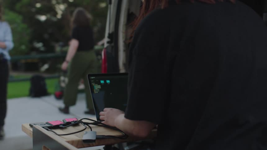 Woman with headphones next to a van working on a laptop