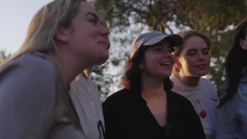 A group of four young adults in a moment of shared laughter outdoors looking at a camera