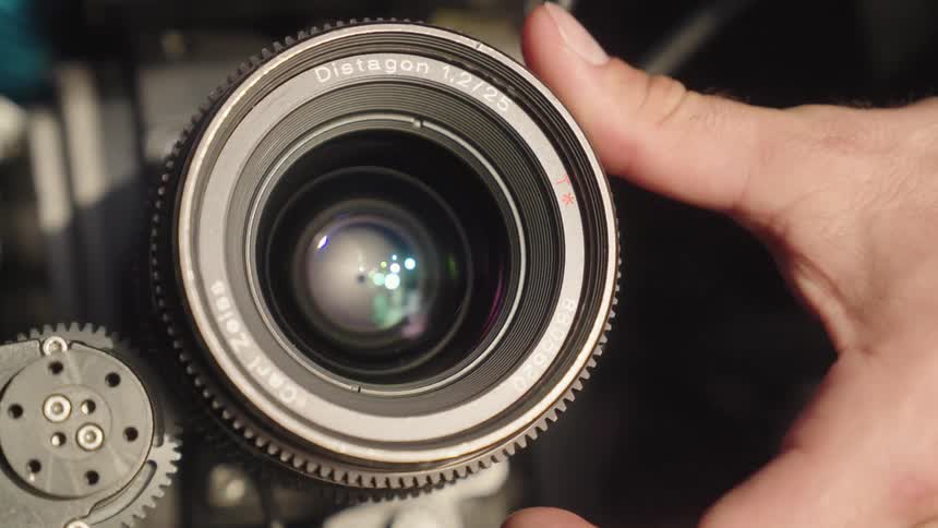 A closeup shot shows a hand carefully turning the geared adjustment ring on a carl zeiss distagon camera lens
