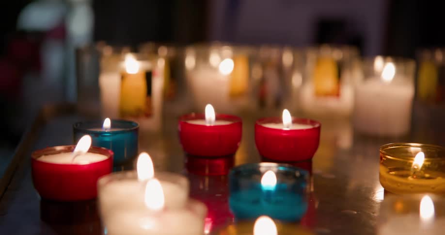 Several candles in small colorful bowls lit on a counter