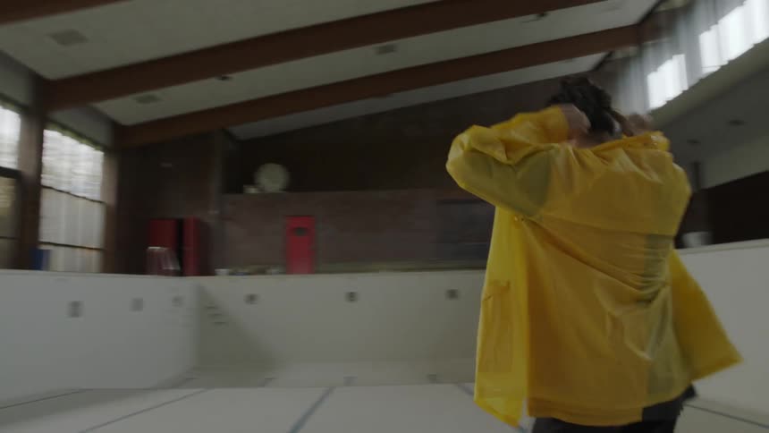 A young woman walks into an empty indoor pool and squats down