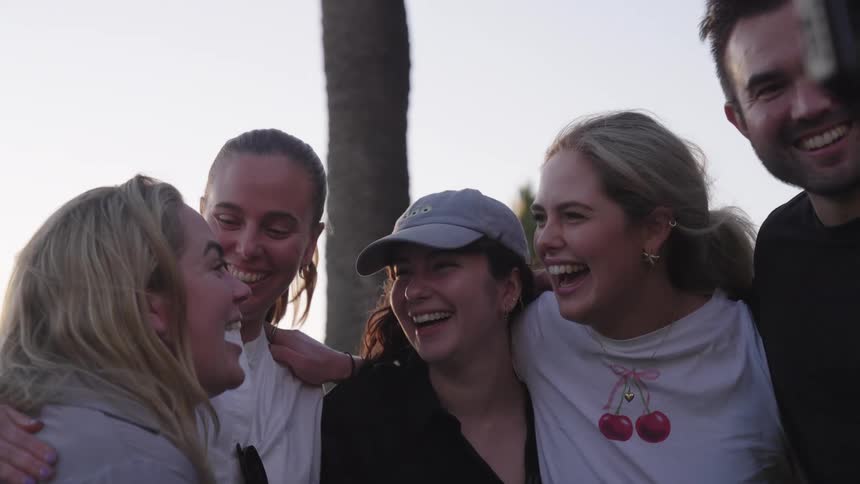 Group of four happy women and one man hugging together and a camera filming