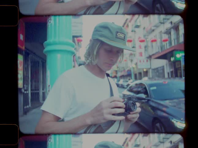 A young man pulls a camera out of his bag while standing on a sidewalk in an urban area