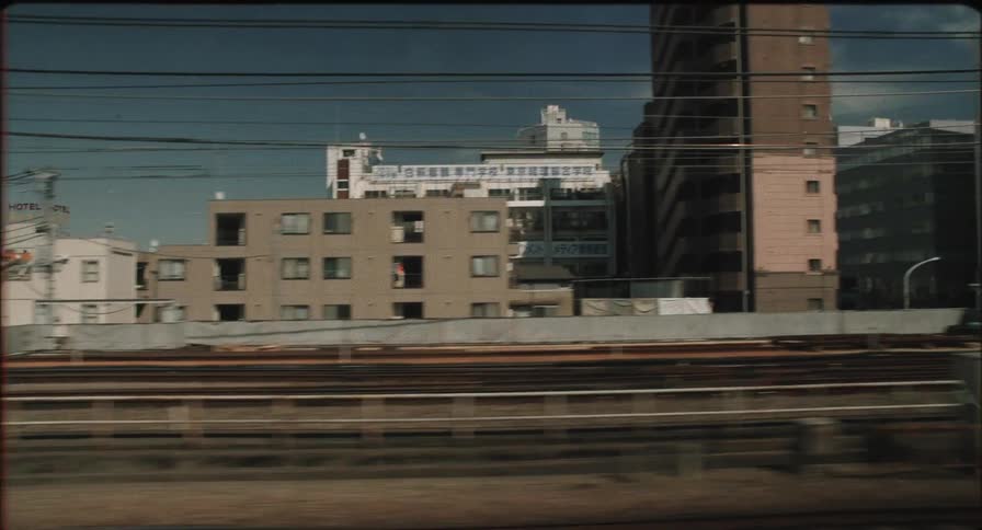 A moving train captures a cityscape with a mix of residential and commercial buildings railway tracks in the foreground