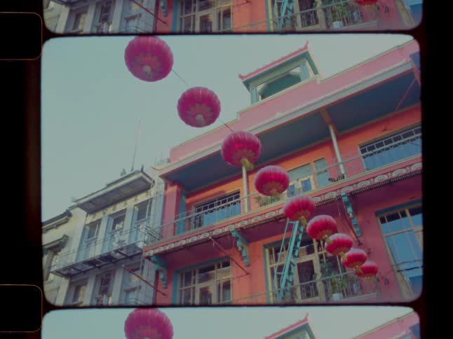 Bright pink paper lanterns hang across a street near a pink apartment building