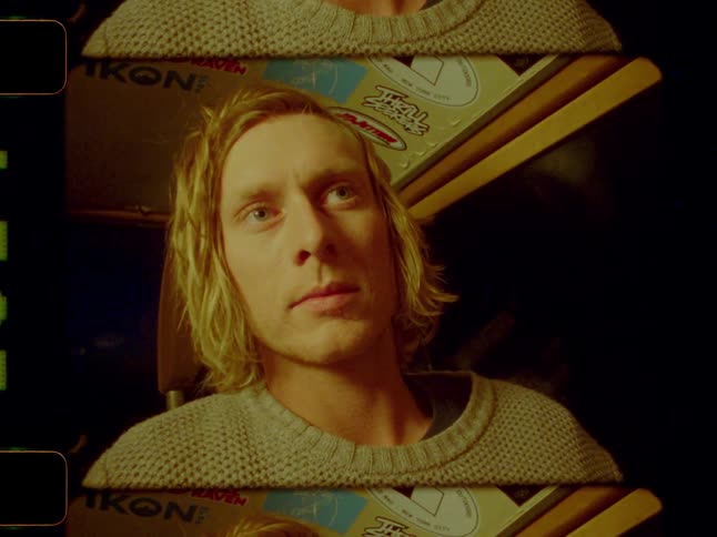 A young blonde man in a sweater looking around a warmly lit interior