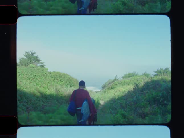 Man with a surfboard walks on a trail towards the sea