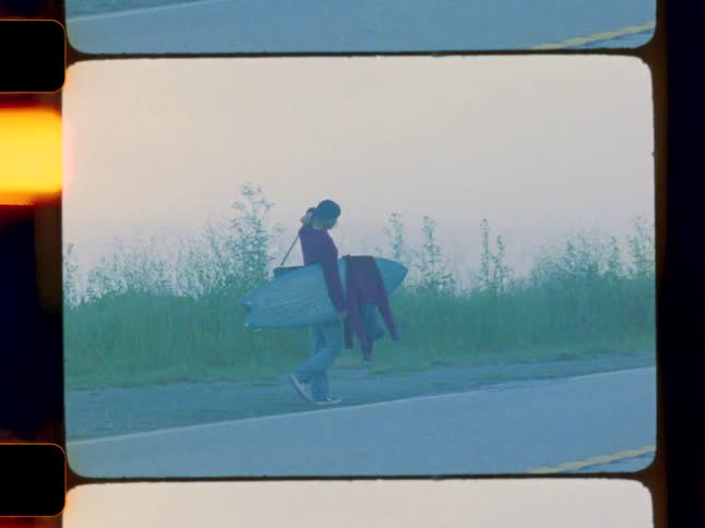 Man walking on the side of the road in a natural environment with a surfboard