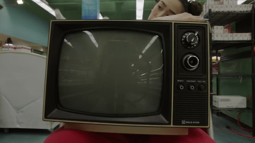 A woman holding a tv is sitting in the middle of an aisle in a grocery store