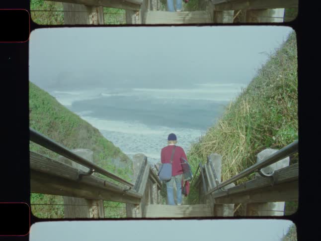 Man with a surfboard walking down the stairs towards the sea