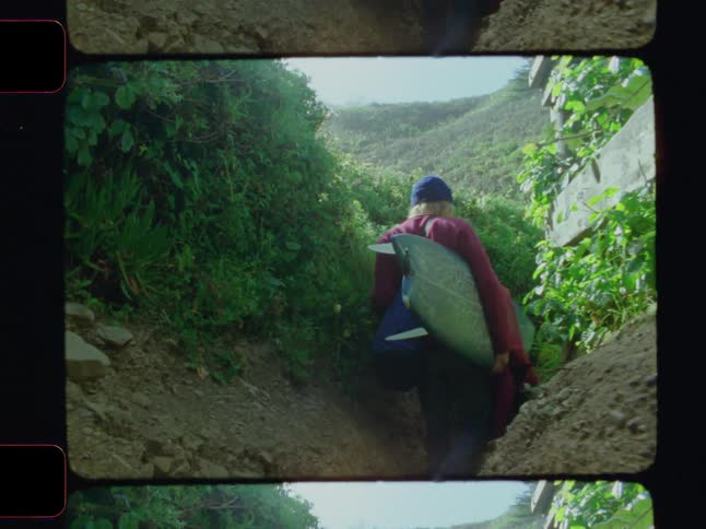 Man with a surfboard walking along a trail
