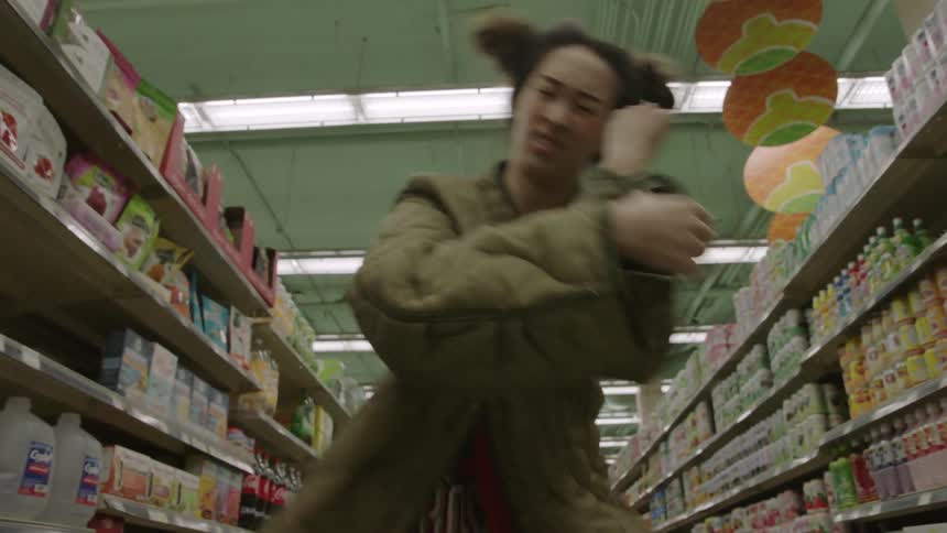 A young asian woman is dancing in a grocery aisle