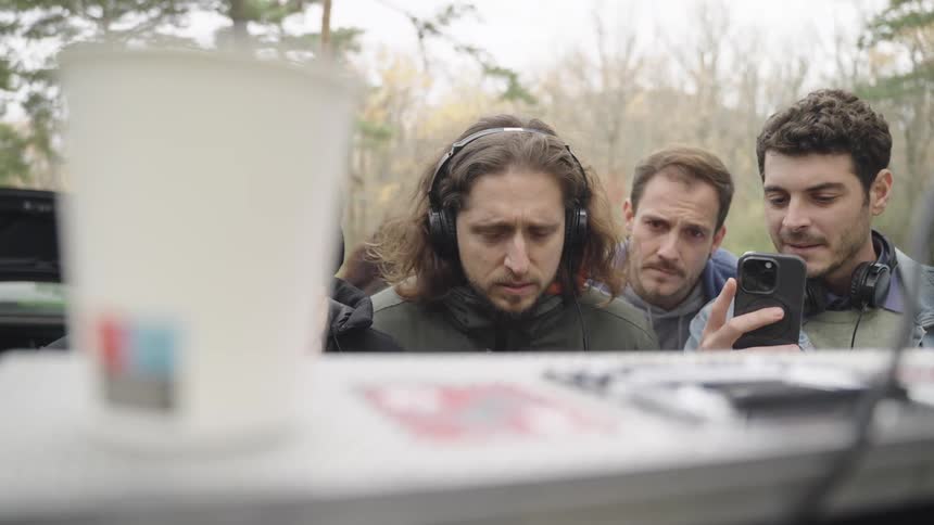 Four men outdoors in a forest looking at recording equipment on a set