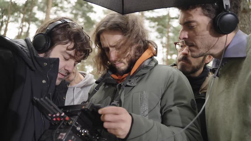 Group of men on an outdoor filming set watching a screen in concentration