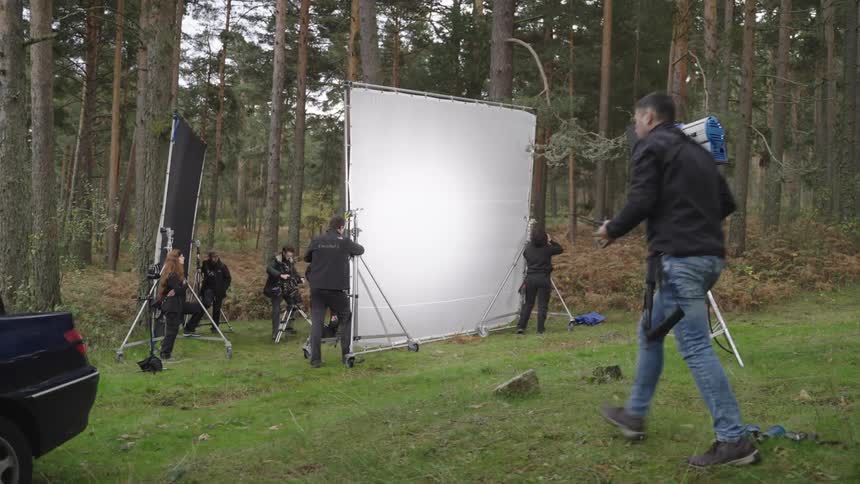 Production crew setting up screens in the forest for a film shoot