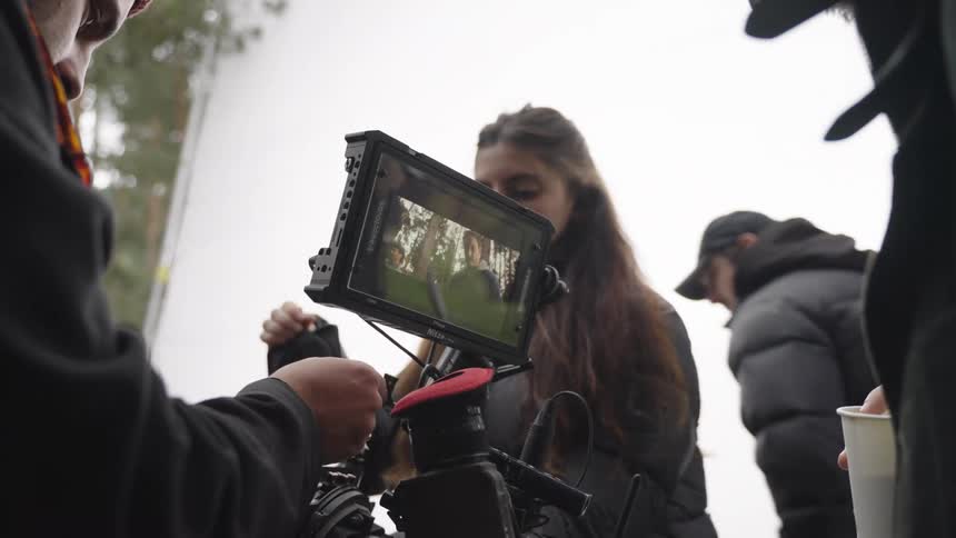 Crew of men and women on an outdoor recording set operating professional video camera