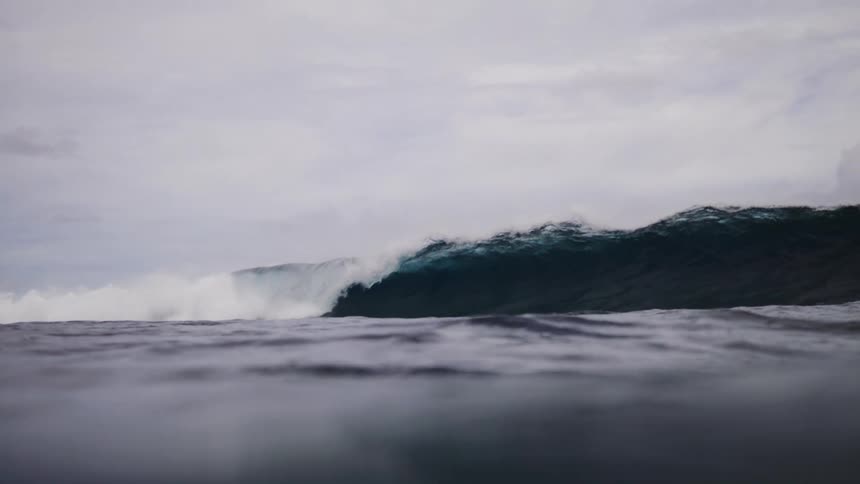 A large sea wave breaking on the surface of the water on a cloudy day