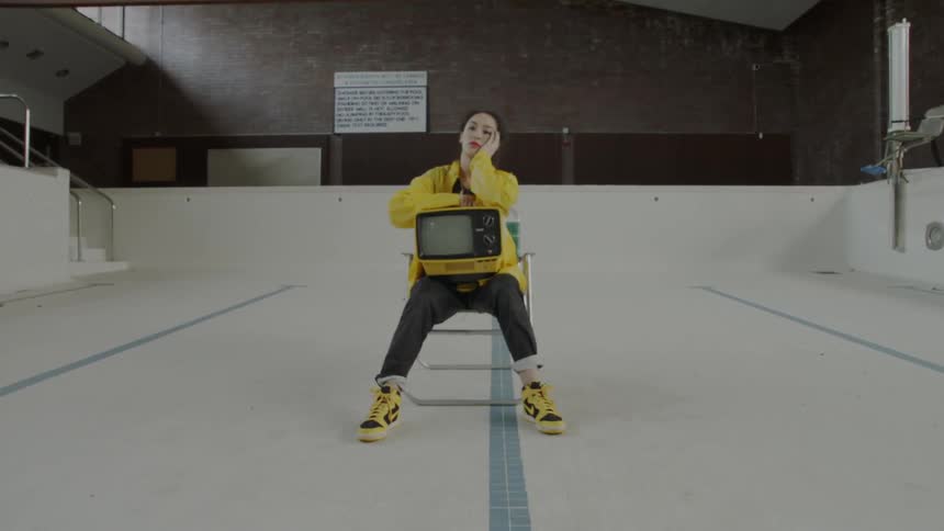 Woman sits on a chair in an empty pool with a tv on her lap